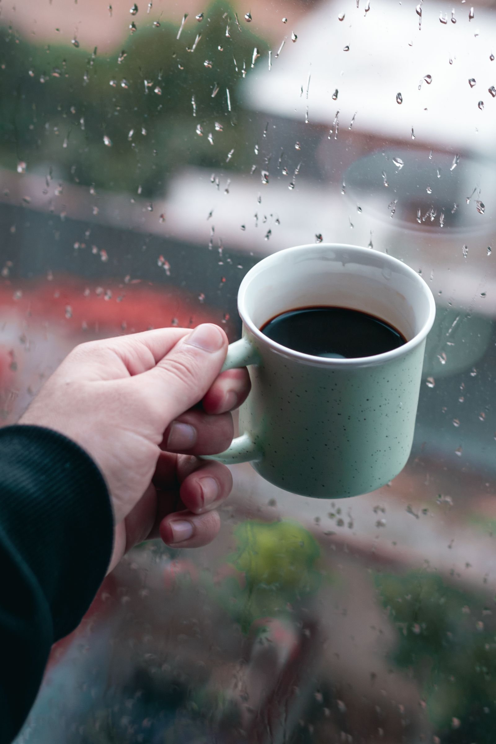 Mão segurando uma xícara junto a uma janela com chuva, clima de tensão